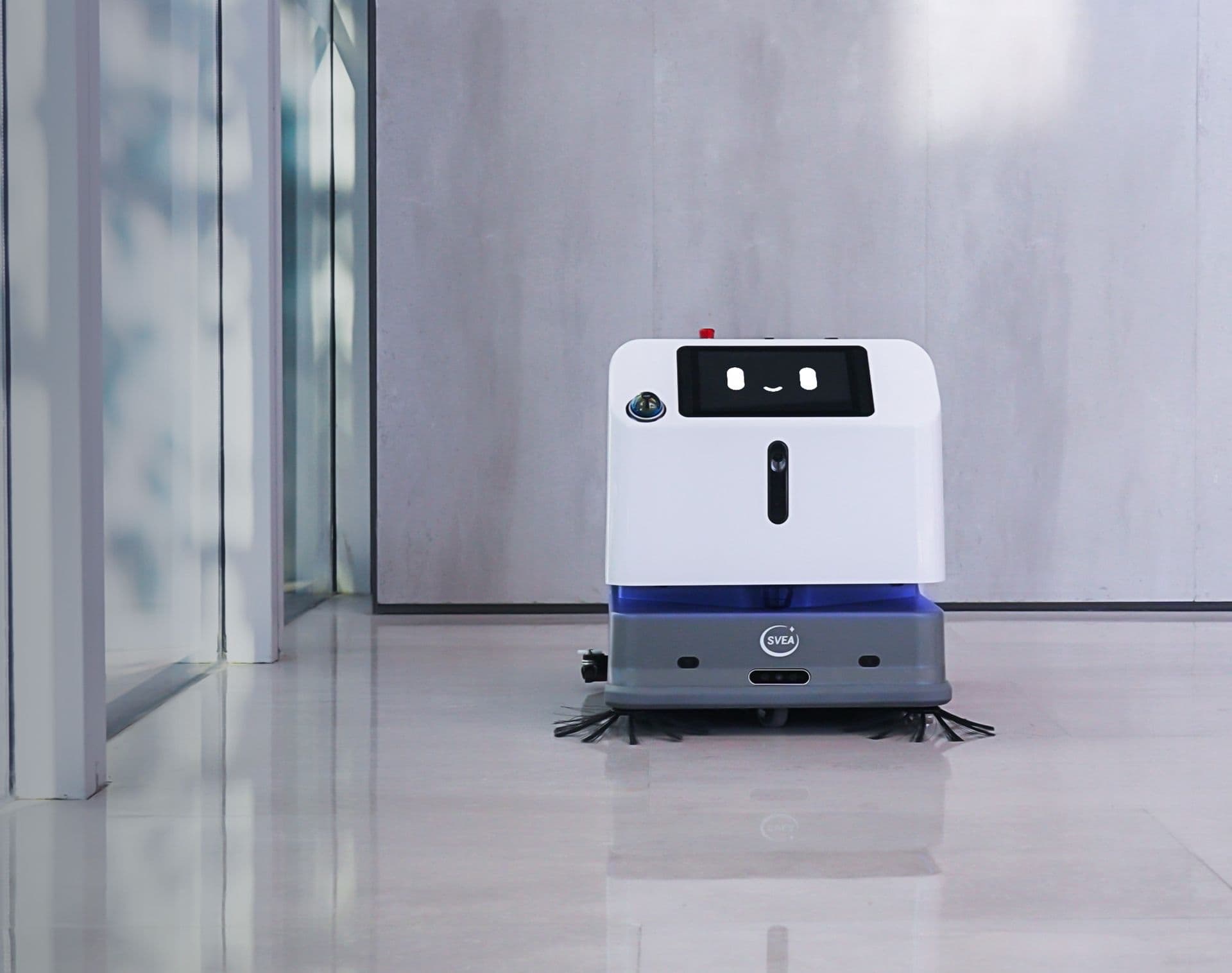 Robot de nettoyage Sveabot S100 Pro R près d’une paroi vitrée dans le hall d’un immeuble de bureaux