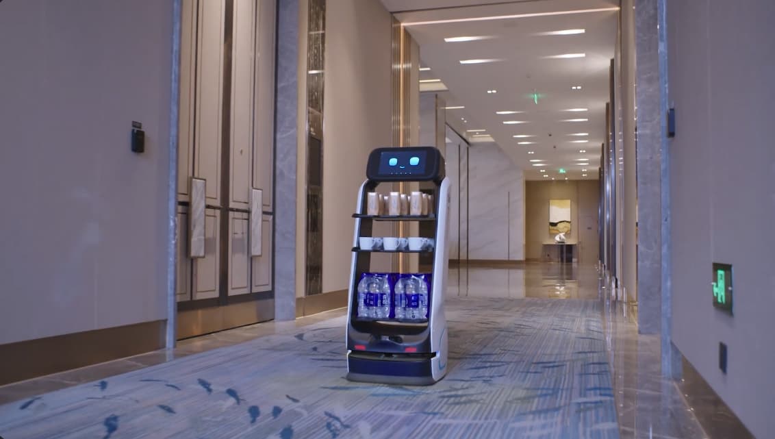 T9 carrying bottled water and cups along a hotel corridor